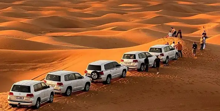Five-Cars-parked-on-desert-sand-dunes-with-people-standing-nearby